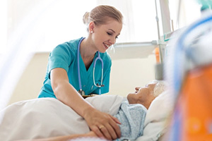 Smiling nurse leaning down to tuck a blanket around a patients shoulders.