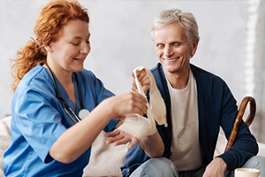 Nurse with bright red hair wrapping a bandage around a patients wound on her wrist.